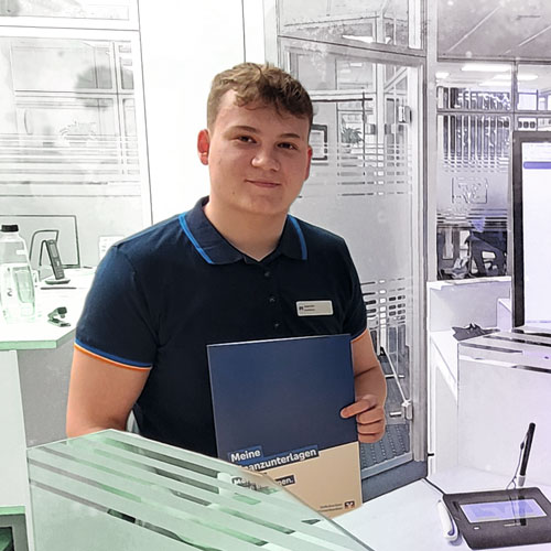 Male receptionist or staff member standing at a service desk, holding a blue folder, in a modern office environment.