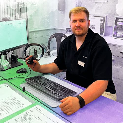 Male staff member with headset at a service counter, seated at a computer with papers and a keyboard ready to assist customers.